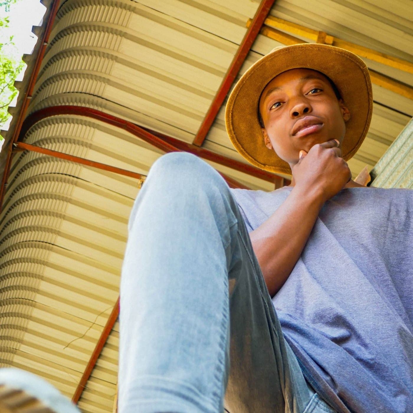 Takue SBT seen from below, in a mustard bucket hat under a corrugated roof